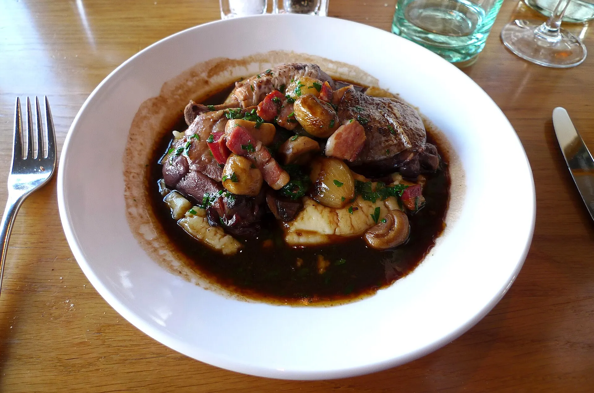 Symbolbild: Coq au vin mit Perlzwiebeln und Rotweinsauce in weißem Teller