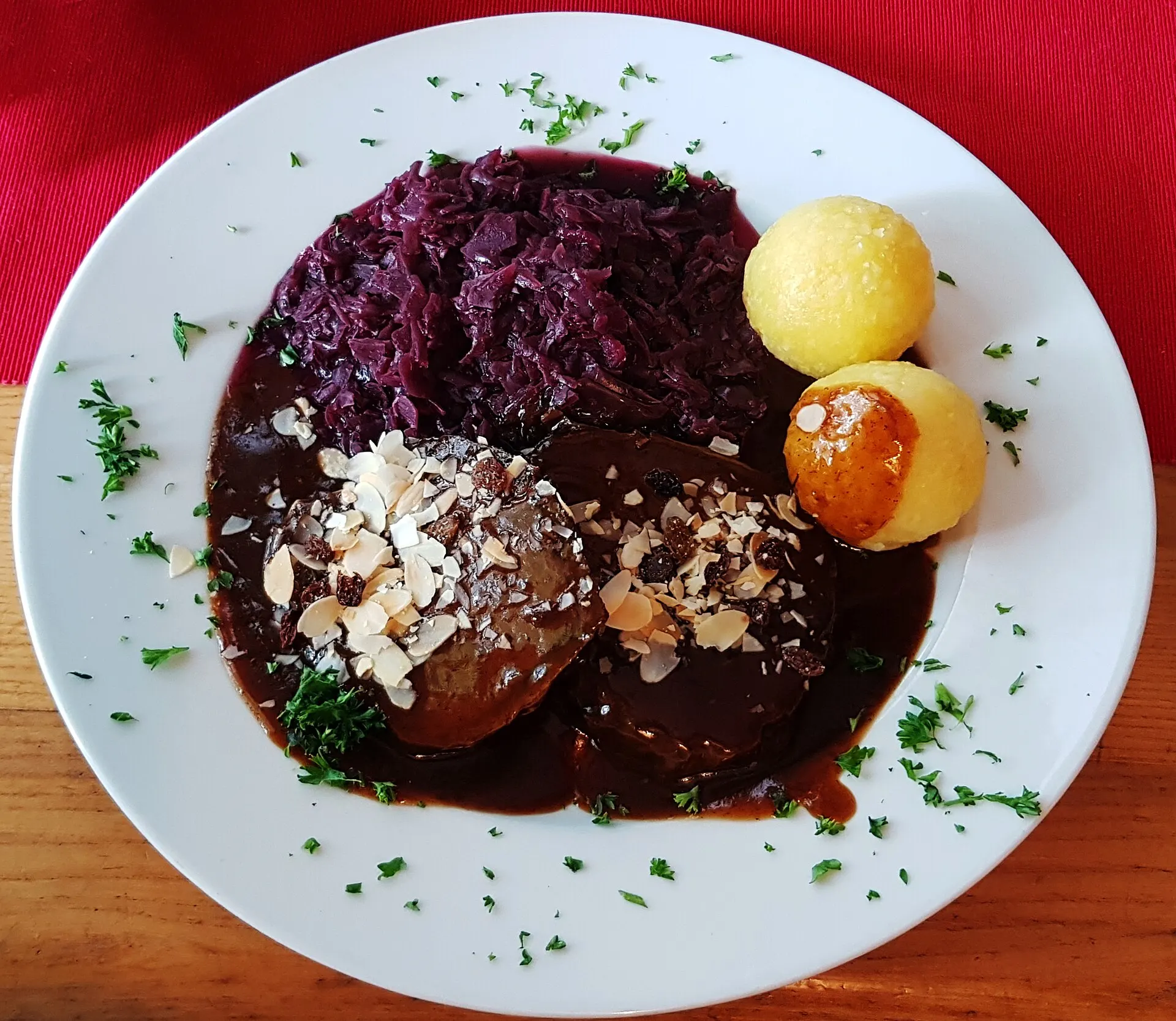 Symbolbild: Sauerbraten mit Rotkohl, Klößen und dunkler Soße auf weißem Teller